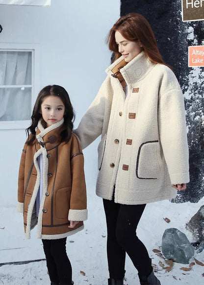 Stylish family in matching shearling jackets, standing in front of a snow-covered wooden cabin during winter