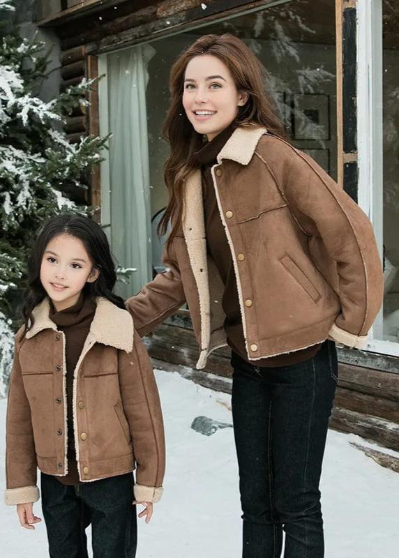 Happy family in matching brown shearling jackets and dark pants, holding hands and smiling in a snowy winter landscape