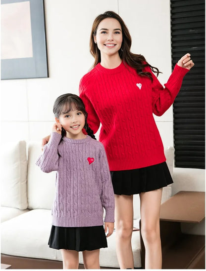 Happy family wearing matching cable knit sweaters in red, grey, white, and purple with heart details, perfect for holiday photos