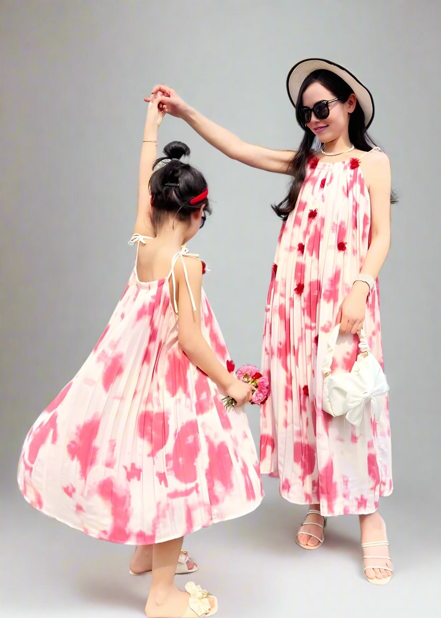 Mother and daughter in matching pink and white tie-dye dresses holding hands